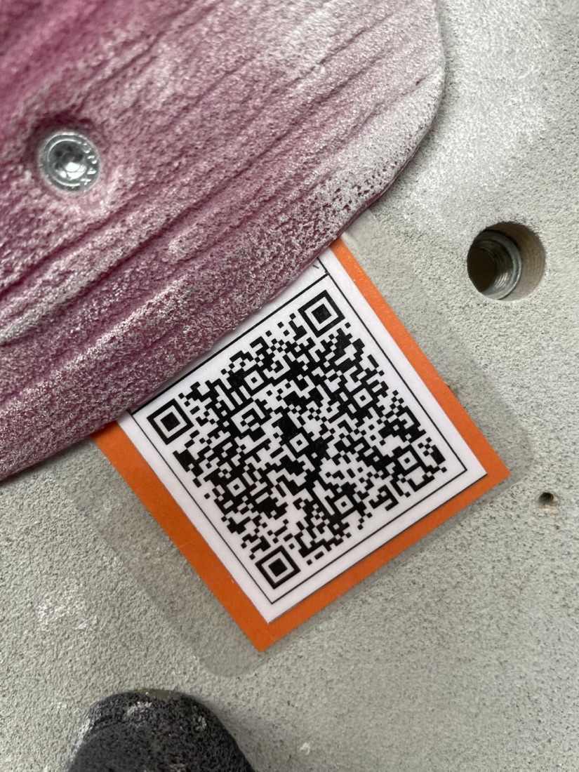 An inClimb QR code sticker on a climbing wall, next to a pink hold